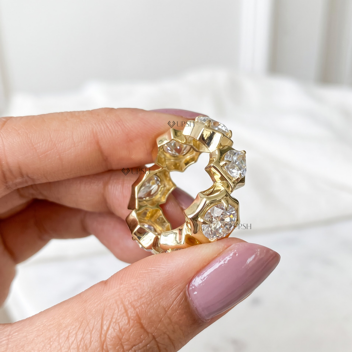 Hand close-up holding wide yellow gold sculpted bezel diamond eternity ring