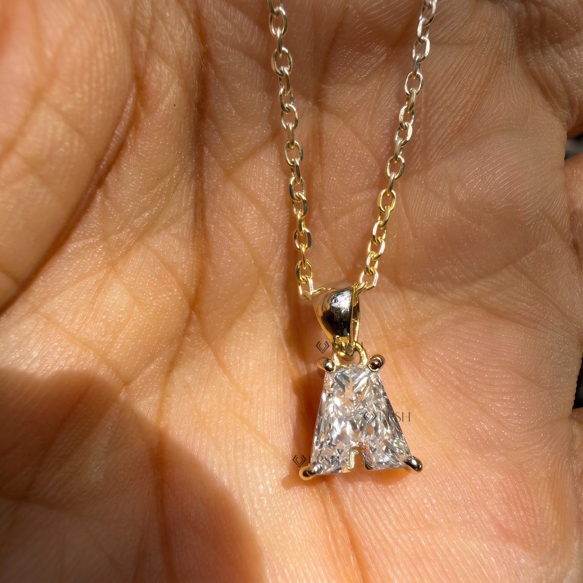 Detailed hand model view of solid yellow gold letter A diamond initial pendant held between fingers