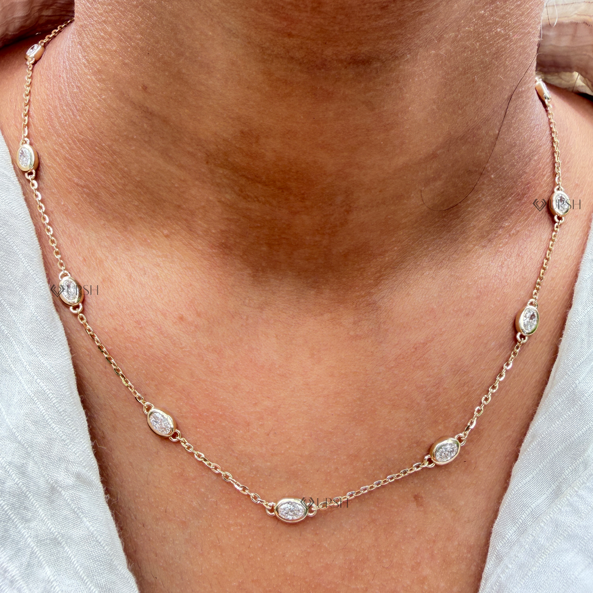 Daylight perspective view of yellow gold floating oval diamond station chain necklace worn along collarbone