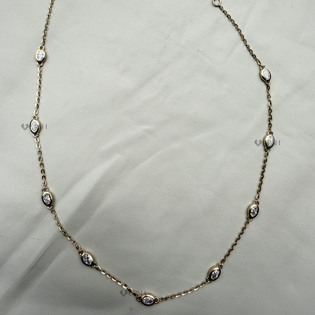 Solid white gold bezel set oval diamond station chain necklace laid flat on neutral background