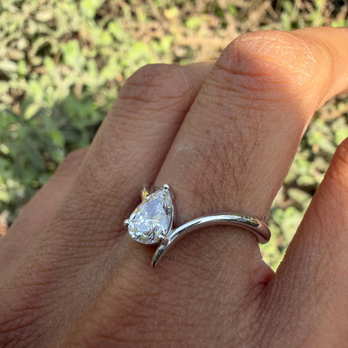 Side angle showing fluid bypass curve and raised prong setting of pear diamond ring on hand