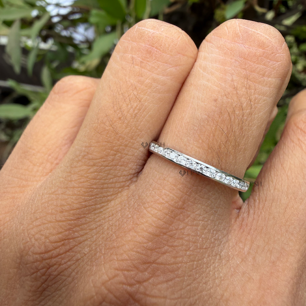 A close-up of a hand wearing a thin silver band ring set with small clear stones, photographed outdoors with blurred green foliage in the background.