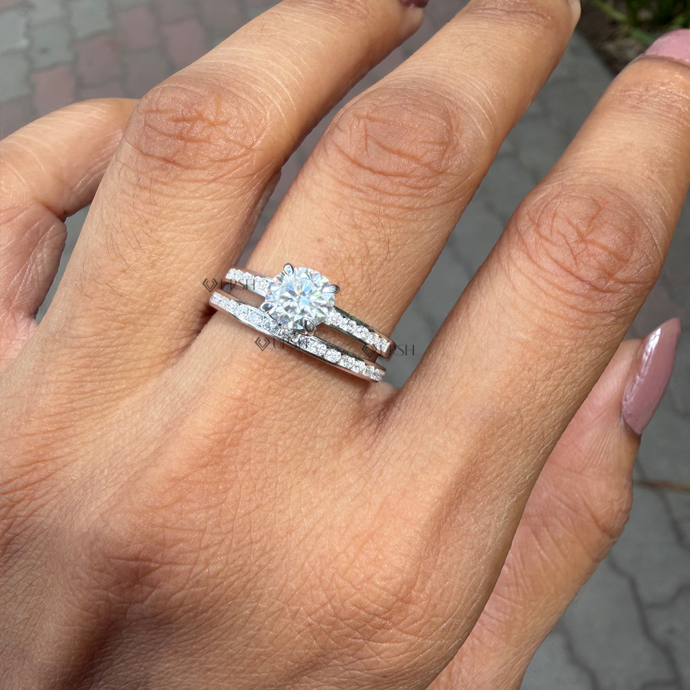 A close-up of a hand wearing a silver-toned double-band ring with a large round-cut center stone and small pavé accents, photographed outdoors on a paved surface.