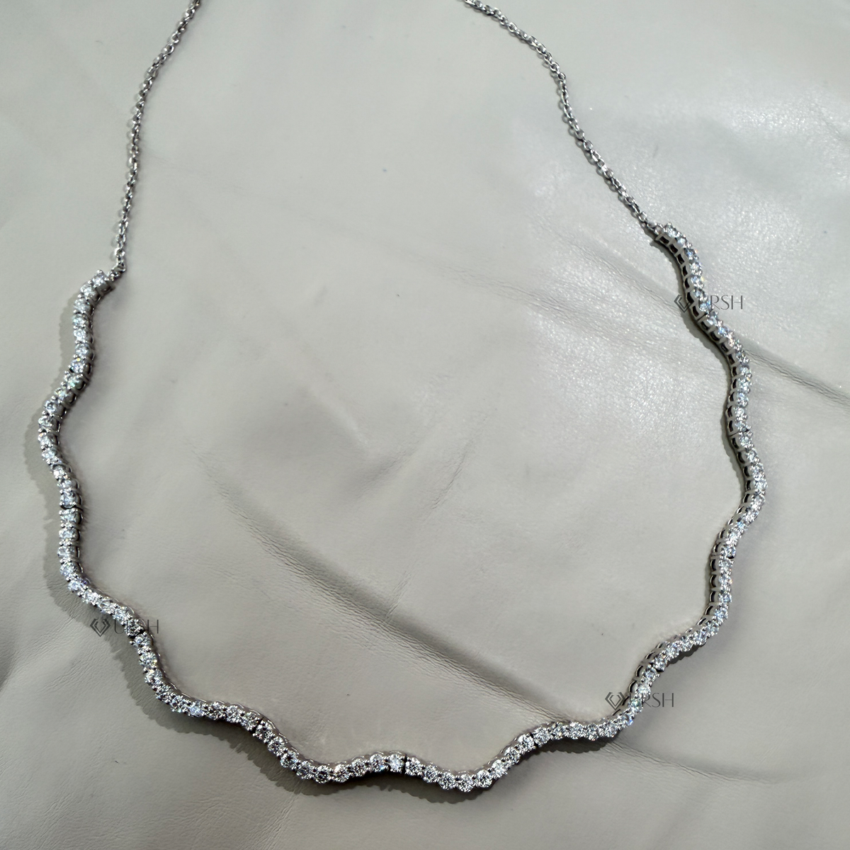 Solid white gold wavy diamond tennis chain necklace laid flat on neutral background