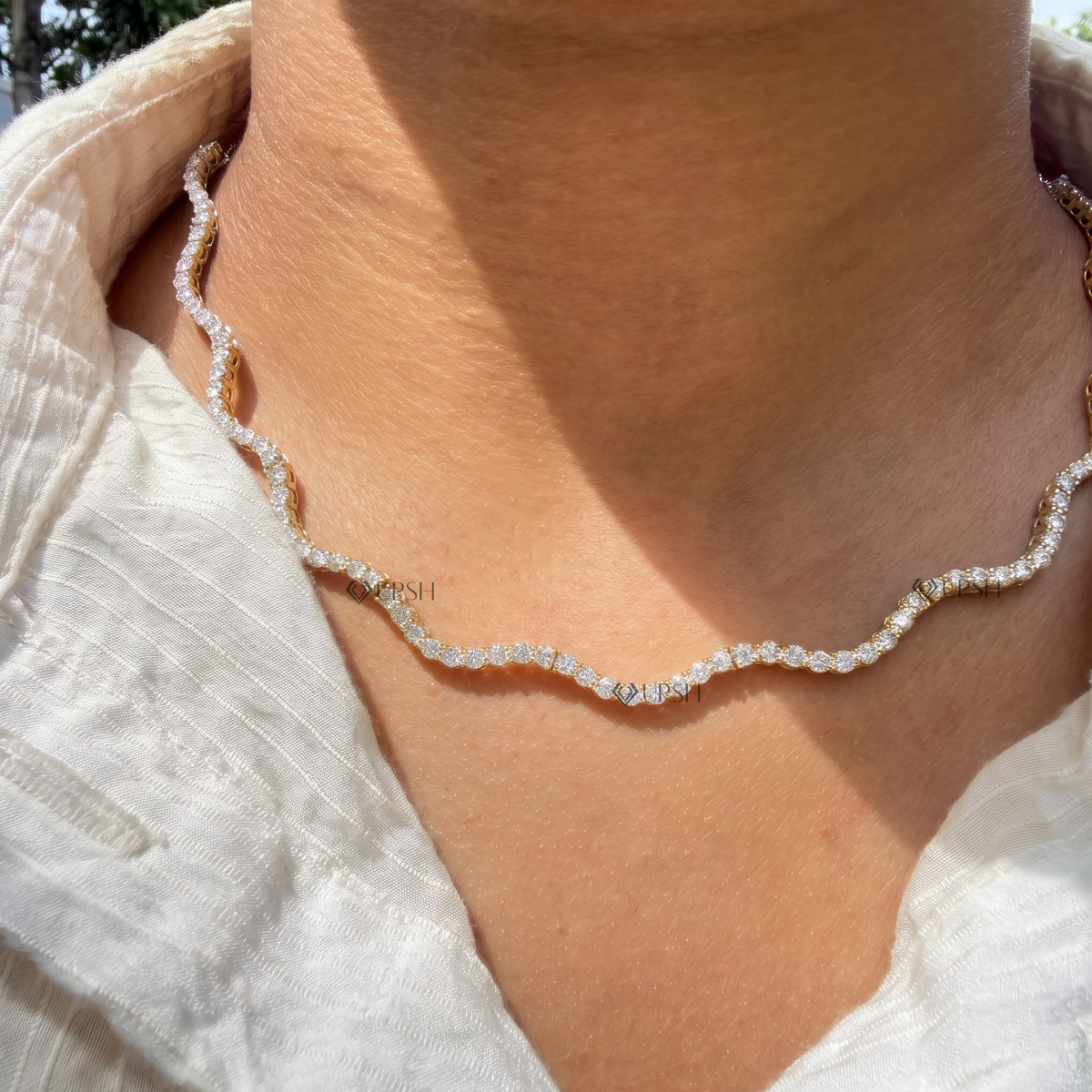Daylight perspective of yellow gold wavy diamond tennis chain necklace worn along collarbone